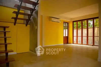 Spacious living room with vibrant yellow walls and modern staircase, featuring large windows for natural light.
