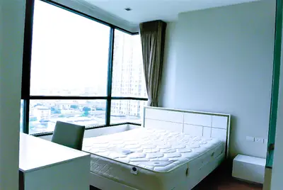 Modern bedroom with large windows offering a stunning city view, featuring a comfortable bed and sleek furniture.