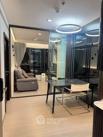 Modern apartment interior with stylish dining area and cozy living room, featuring elegant lighting and glass partitions.