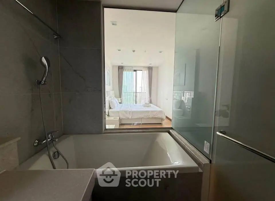 Modern bathroom with bathtub and view into a stylish bedroom, featuring sleek design and natural light.