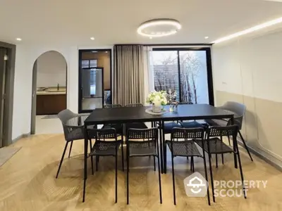 Elegant dining area with modern black table and chairs, featuring stylish lighting and wooden flooring.