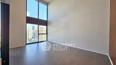 Spacious high-ceiling room with large windows offering stunning city views.