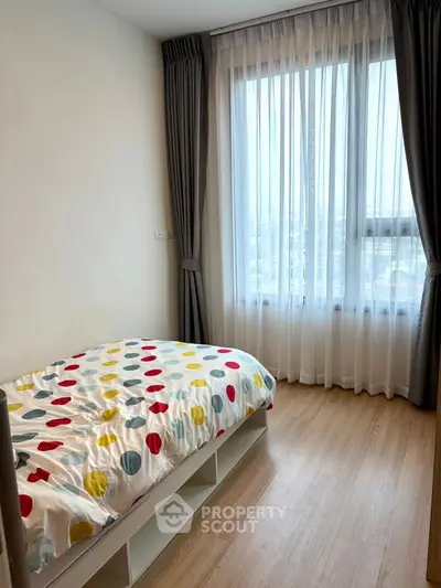 Cozy bedroom with colorful bedding and large window with curtains.