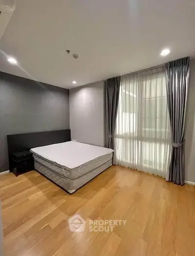 Spacious bedroom with wooden flooring and large window in modern apartment