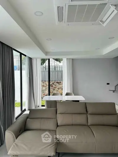 Modern living room with sleek furniture and large windows offering natural light and garden view.
