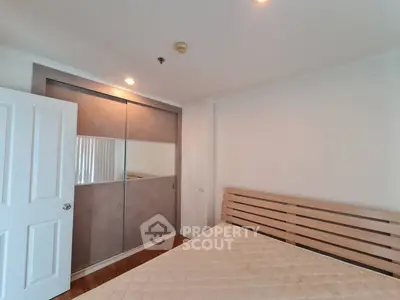 Spacious bedroom with modern closet and wooden bed frame in a bright apartment.