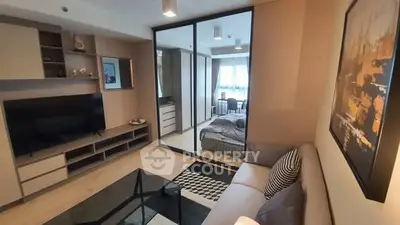 Modern living room with stylish decor and a view into a cozy bedroom, featuring sleek furniture and a large TV.