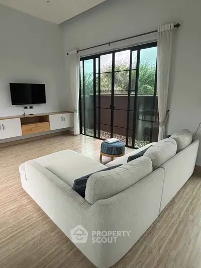 Spacious living room with modern sofa and large glass doors leading to a serene outdoor view.