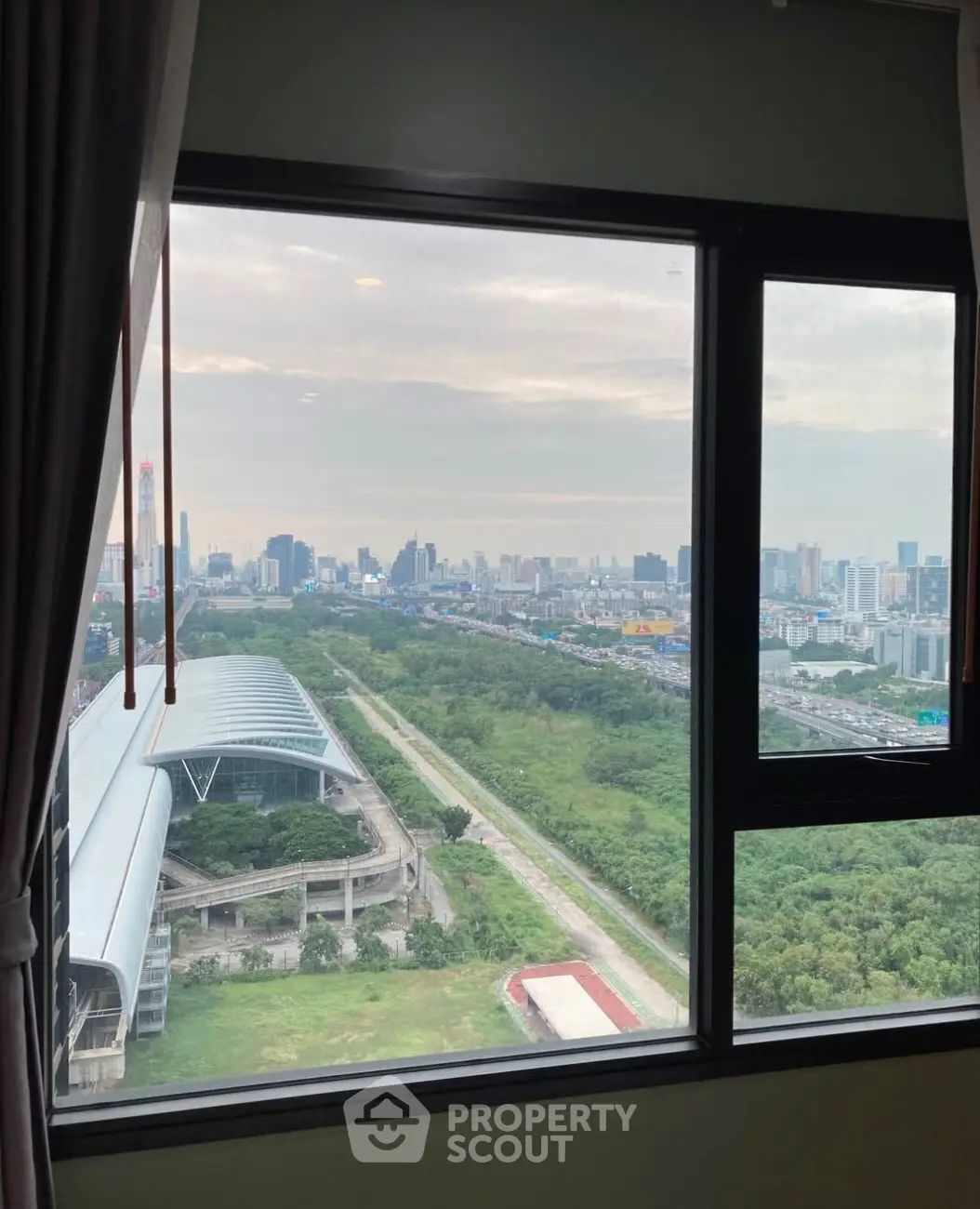 Stunning cityscape view from high-rise apartment window, showcasing urban skyline and lush greenery.