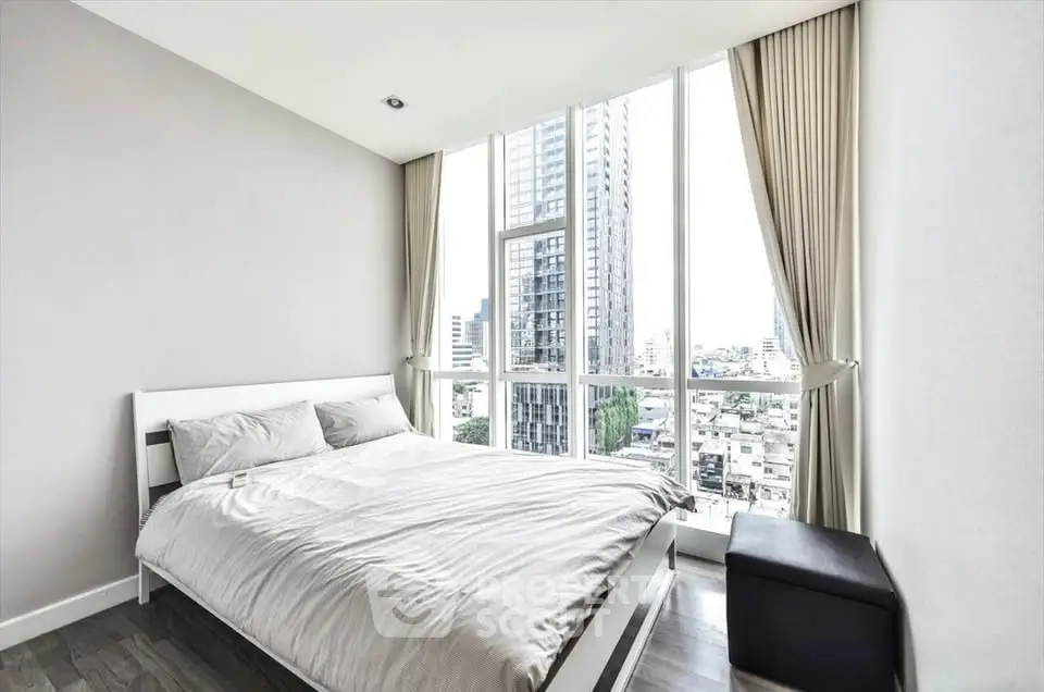 Modern bedroom with large windows offering stunning city views in a high-rise apartment.