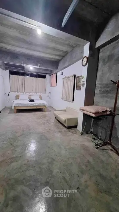 Spacious industrial-style bedroom with minimalist decor and concrete flooring.