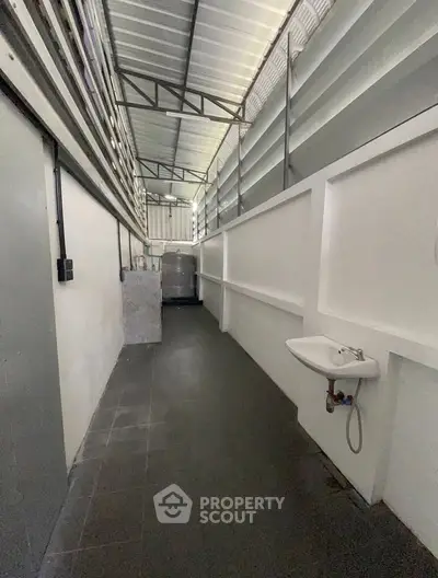 Spacious industrial-style corridor with high ceiling and sink, ideal for storage or utility use.