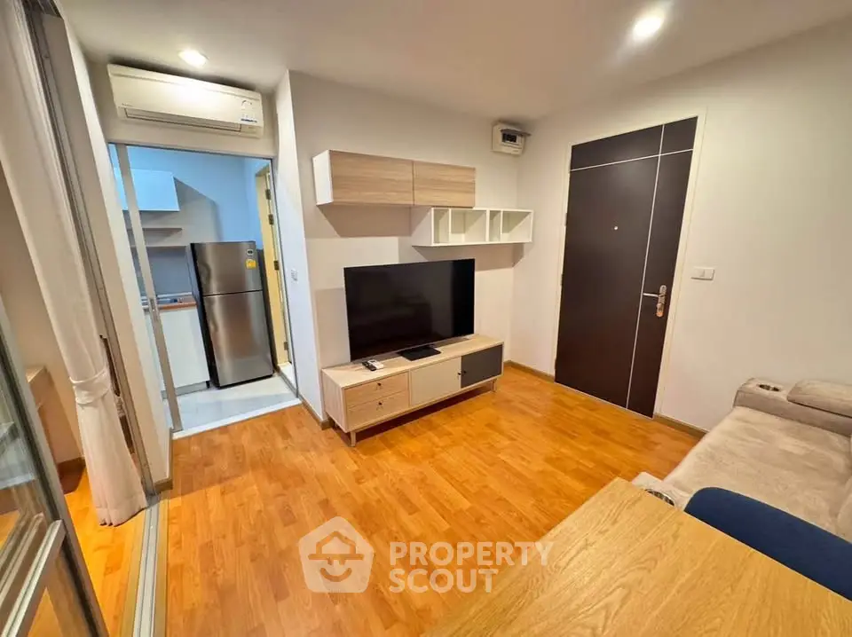 Modern living room with wooden flooring, TV unit, and open kitchen view in a cozy apartment.