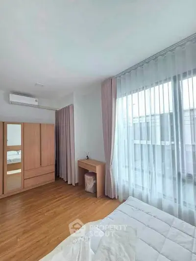 Bright bedroom with wooden flooring, large window, and modern furniture in a stylish apartment.