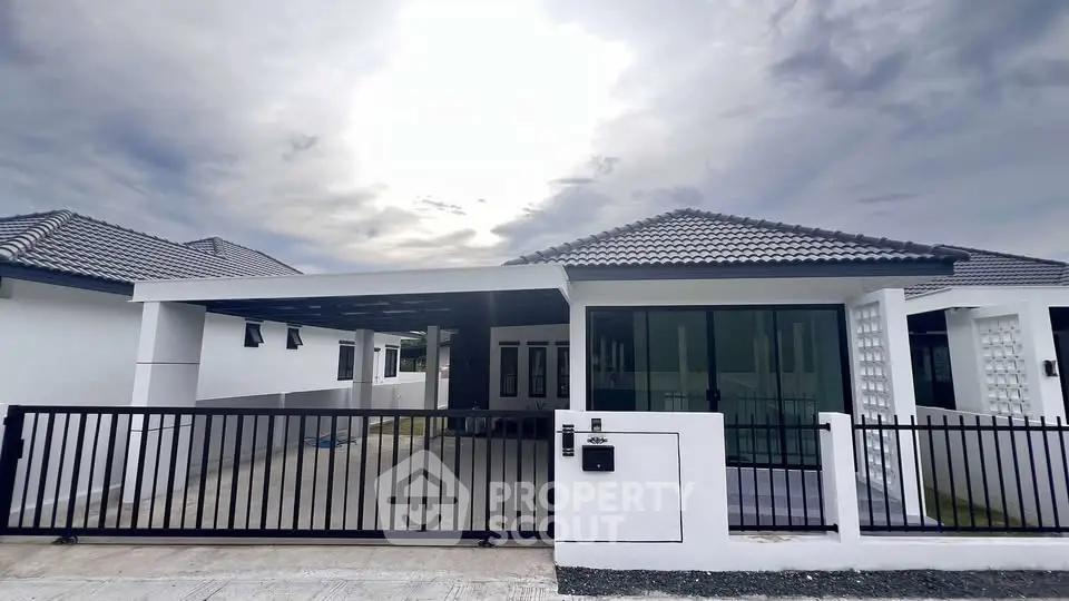 Modern single-story house with sleek design and spacious driveway under a cloudy sky.