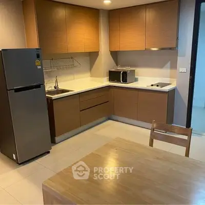 Modern kitchen with wooden cabinets, stainless steel fridge, and microwave in a cozy apartment.