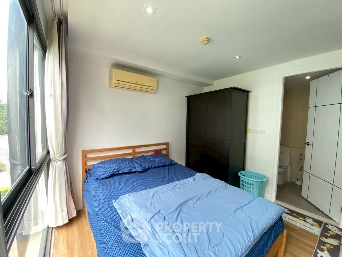 Cozy bedroom with large window and modern air conditioning unit, featuring a comfortable bed and wardrobe.