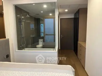 Modern bedroom with glass-enclosed bathroom featuring a bathtub and sleek design.