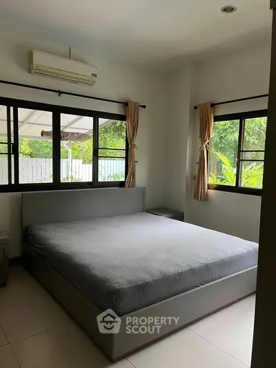 Spacious bedroom with large windows and garden view, featuring a modern bed and air conditioning.