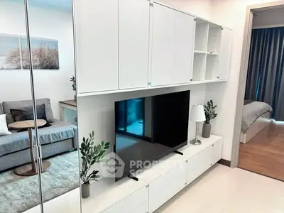 Modern living room with sleek white cabinetry and large TV, adjacent to a cozy bedroom.