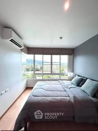 Spacious bedroom with large windows offering scenic views, modern decor, and air conditioning.