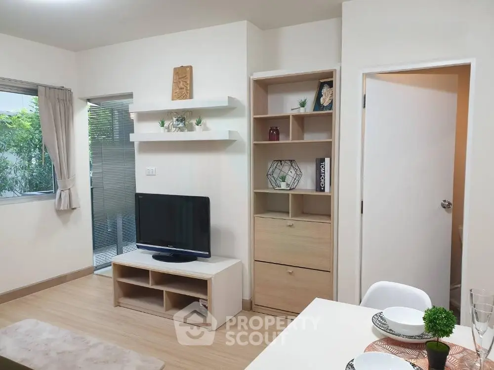 Modern living room with stylish decor and natural light, featuring a TV and elegant shelving.