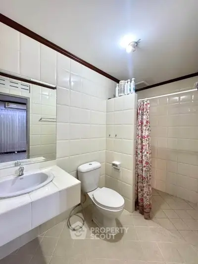 Spacious bathroom with modern fixtures and floral shower curtain in a bright, tiled setting.