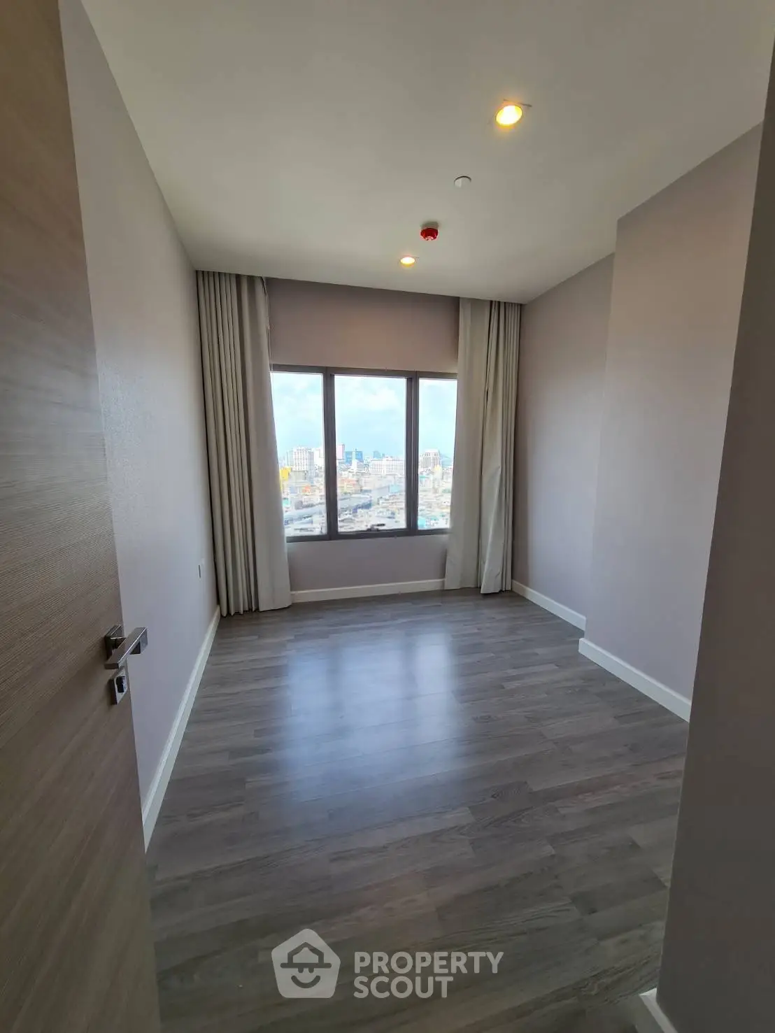 Spacious empty room with large window offering stunning city view, perfect for customization.