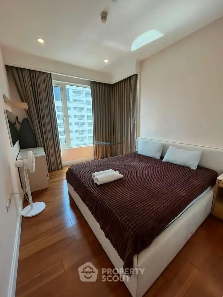 Cozy bedroom with modern decor and large window offering city views, perfect for urban living.