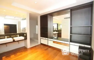 Spacious modern living room with polished hardwood floors, sleek built-in shelving, and a peek into a well-lit kitchen area.