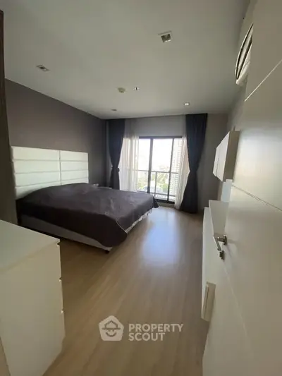 Spacious bedroom with large window and modern decor in a stylish apartment.