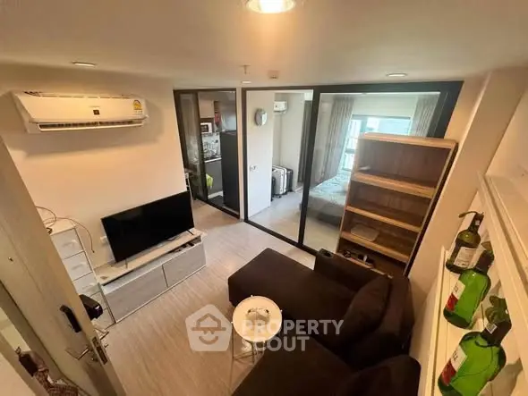 Modern living room with sleek furniture and glass partition leading to bedroom, featuring air conditioning and stylish decor.