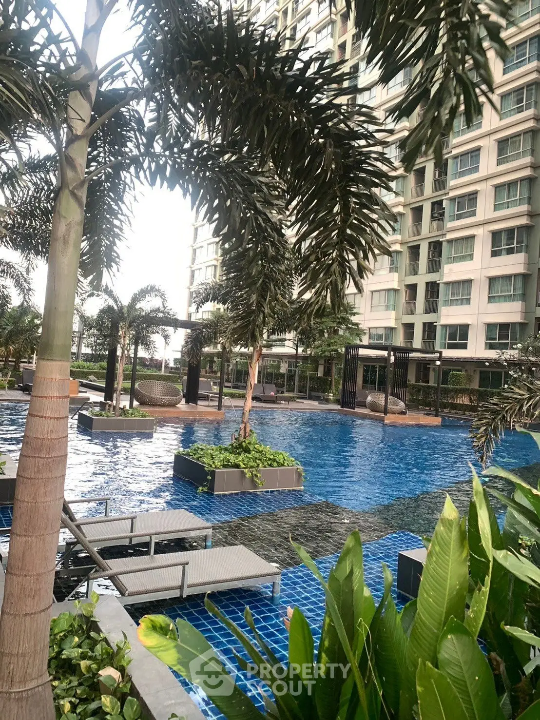 Luxurious residential pool area with lush greenery and modern high-rise backdrop.