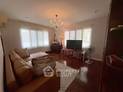 Cozy living room with elegant chandelier and large windows, featuring a comfortable sofa and modern TV setup.