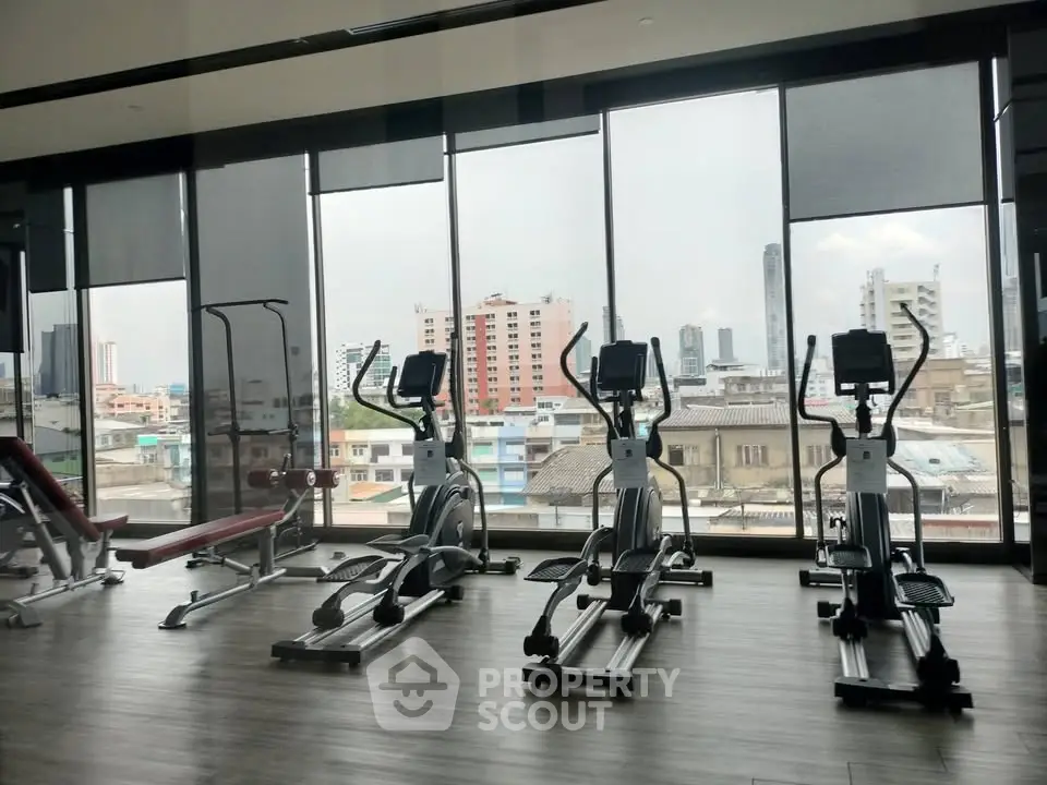 Modern gym with city view in high-rise building, featuring exercise equipment and large windows.