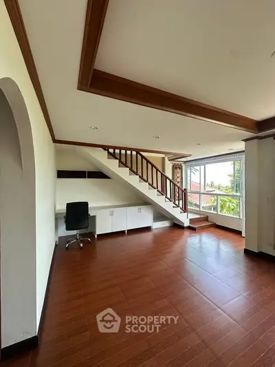 Spacious living room with wooden flooring and staircase, featuring large windows for natural light.