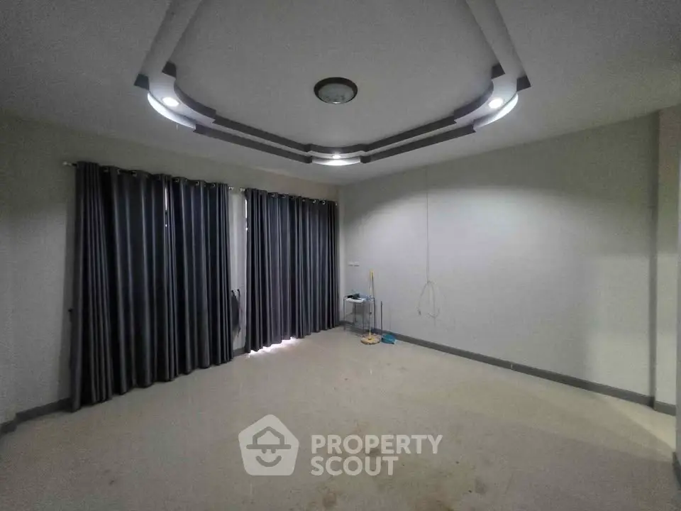 Spacious empty room with modern ceiling design and large windows with curtains.