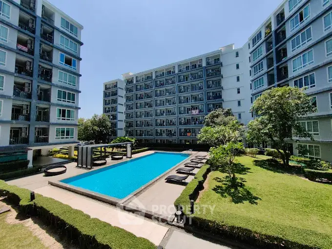 Modern apartment complex with pool and landscaped garden under clear blue sky.