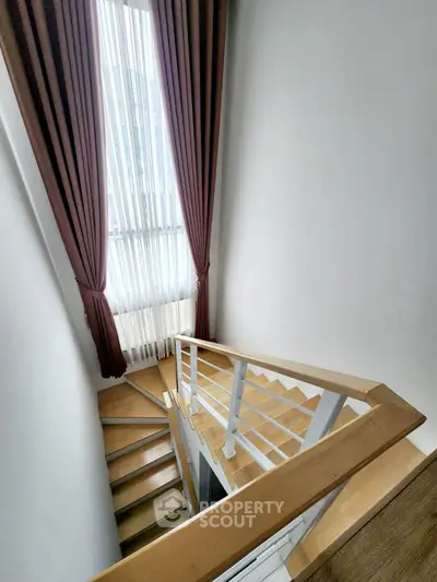 Elegant staircase with wooden steps and modern railing, featuring floor-to-ceiling window with stylish curtains.