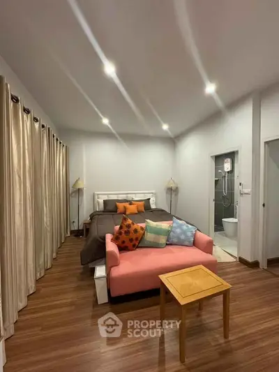 Cozy bedroom with modern decor and ensuite bathroom, featuring a stylish pink sofa and wooden flooring.