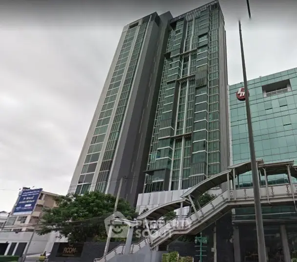 Modern high-rise building with glass facade and adjacent skywalk in urban setting.