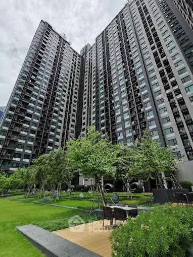 Modern high-rise building with lush green garden and outdoor seating area.