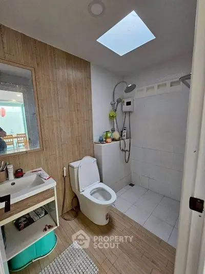 Modern bathroom with skylight and wooden accents, featuring a shower and sleek fixtures.