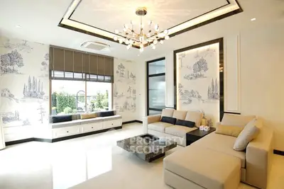 Luxurious living room with elegant chandelier and large windows offering natural light and garden view.