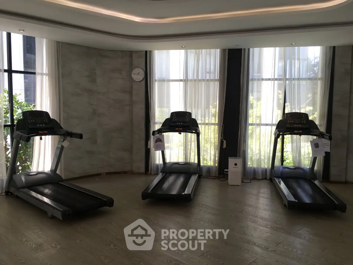 Modern gym with three treadmills and large windows offering natural light.