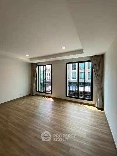Spacious modern living room with large windows and wooden flooring in a contemporary apartment.