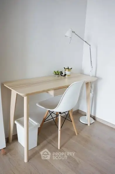 Minimalist study area with wooden desk, white chair, and modern lamp on light wood flooring.