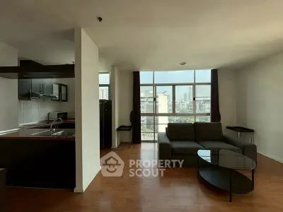 Spacious living room with modern kitchen and city view, featuring sleek furniture and large windows.