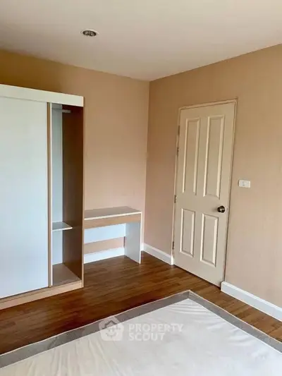 Spacious bedroom with wooden flooring and built-in wardrobe in modern apartment.
