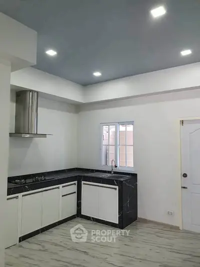 Modern kitchen with sleek black countertops and white cabinetry, featuring a gas stove and ample lighting.